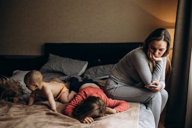 A mom sitting on a bed, sadly watching her three kids.