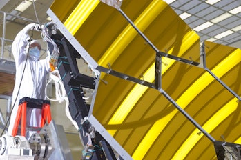 color photo of technician in white suit working on gold hexagonal telescope mirrors