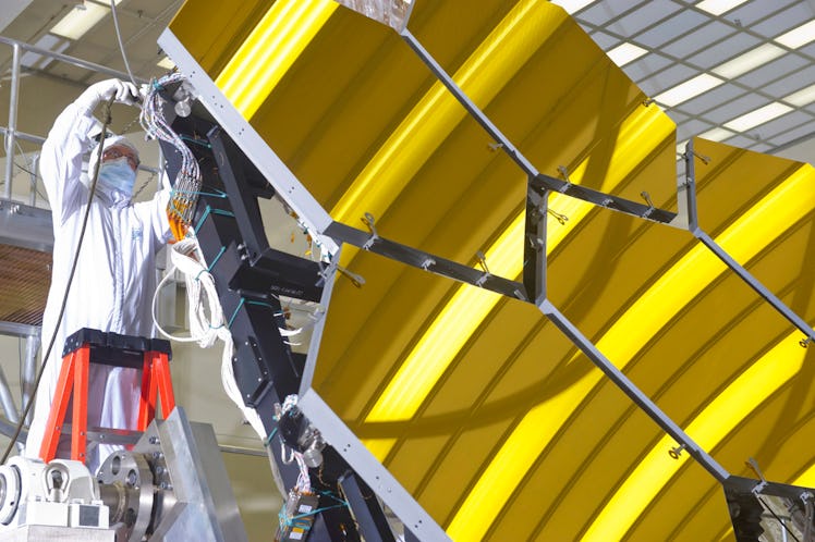 color photo of technician in white suit working on gold hexagonal telescope mirrors