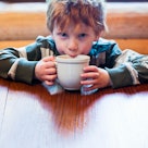 Young boy with light brown hair drinking cocoa at table