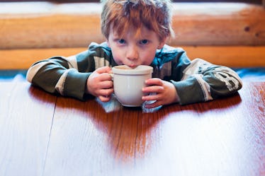 Young boy with light brown hair drinking cocoa at table