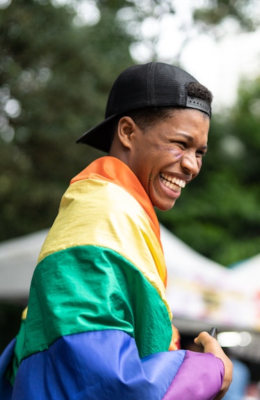 A boy smiling while wrapped in a rainbow flag.
