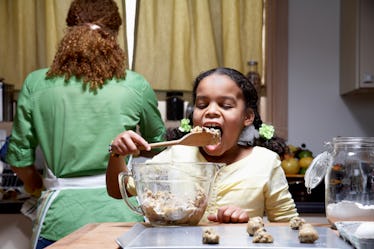 A mother and daughter making cookies together, as the mother's back is turned the daughter eats the ...