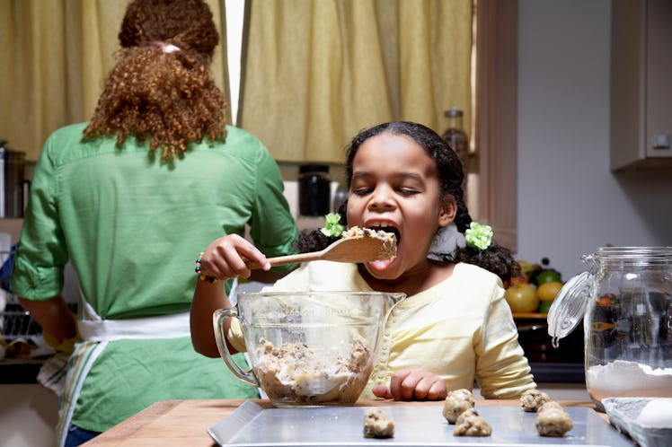 A mother and daughter making cookies together, as the mother's back is turned the daughter eats the ...