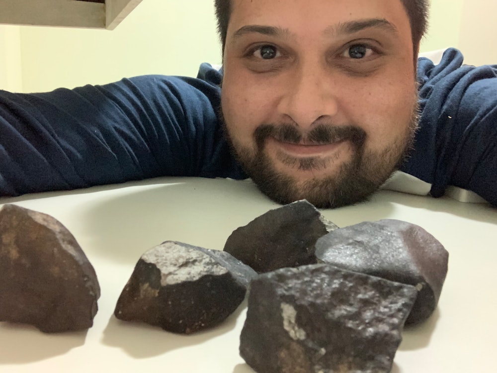 Roberto Vargas grins at the camera with several meteorites on the table in front of him