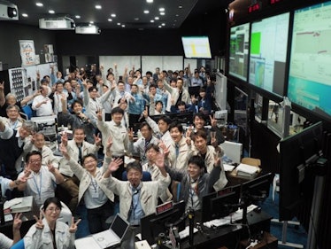 a group of japanese planetary scientists celebrating in a mission control room