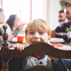 A child turned around on their chair during family dinner smiling at the camera