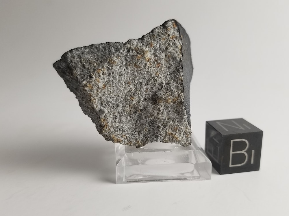 A slab-gray meteorite on a small, clear plate with a cube that says B1 next to it.