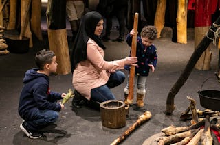 A woman shows her children how the Pawnee, a tribe of Native Americans, grind corn at the Field Muse...