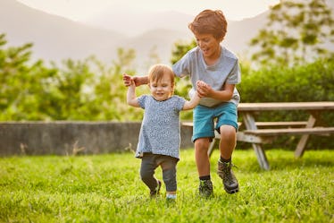 一个哥哥在外面的草地上帮助一个蹒跚学步的孩子。