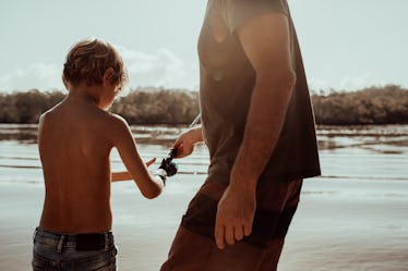 A father helping his son fish at a lake.