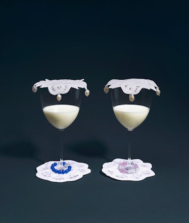 two wine glasses filled with milk, sitting on lace coasters and covered with pearl-trimmed coasters