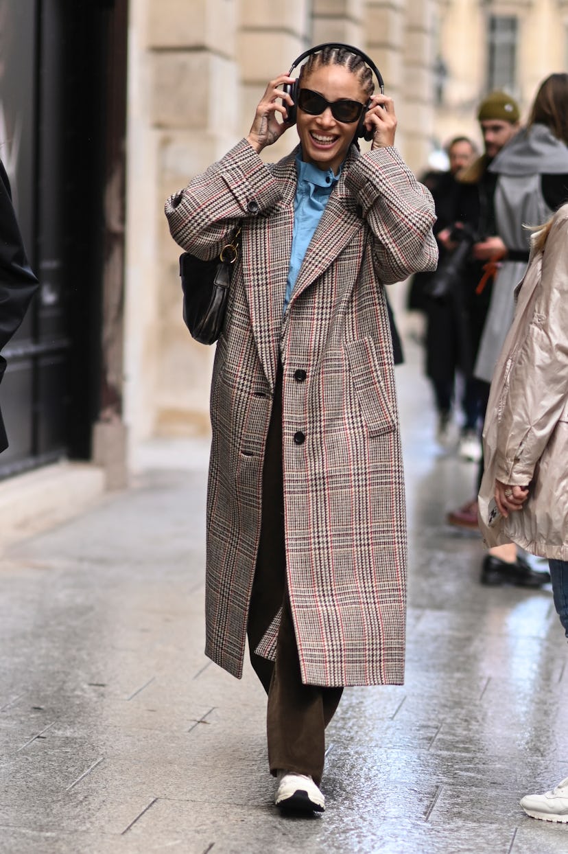 Adwoa Aboah is seen wearing a plaid coat, blue shirt, brown pants, black sunglasses and off-white sn...