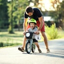 A dad helps his child ride a bike.