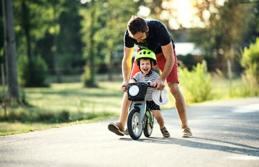 A dad helps his child ride a bike.