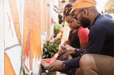 A child and her father volunteer by painting a wall mural.