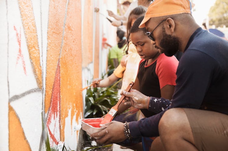 A child and her father volunteer by painting a wall mural.