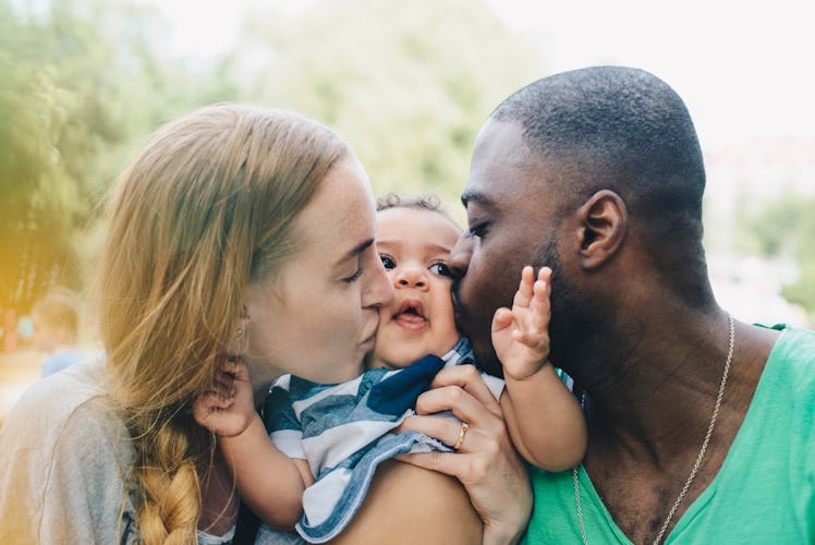 A mom and dad kiss their toddler's cheeks.