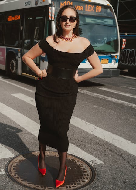 the comedian catherine cohen  standing on a manhole near a crosswalk in New York City, wearing a bla...