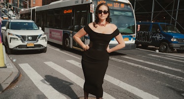 the comedian catherine cohen  standing on a manhole near a crosswalk in New York City, wearing a bla...