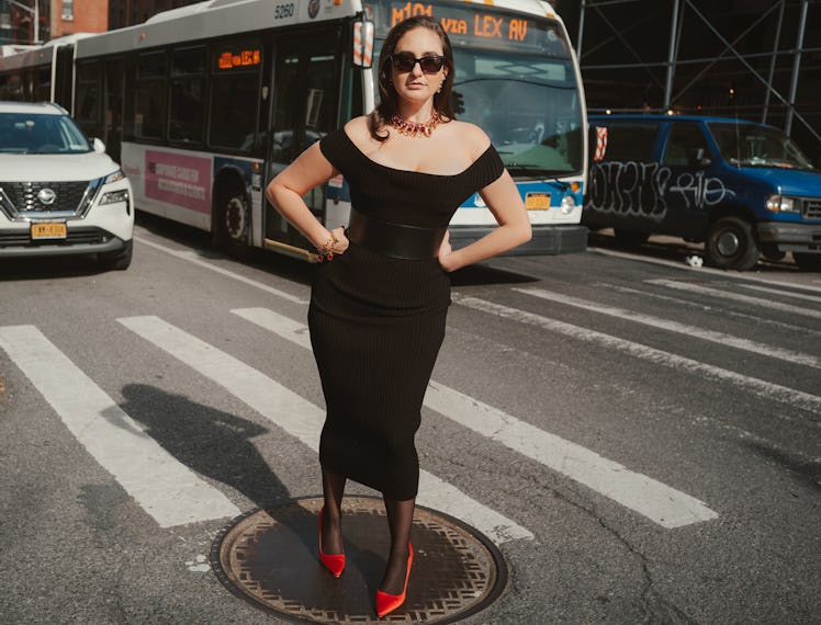 the comedian catherine cohen  standing on a manhole near a crosswalk in New York City, wearing a bla...