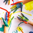 Children's hands with colorful paint on them, above a finger-painted background.