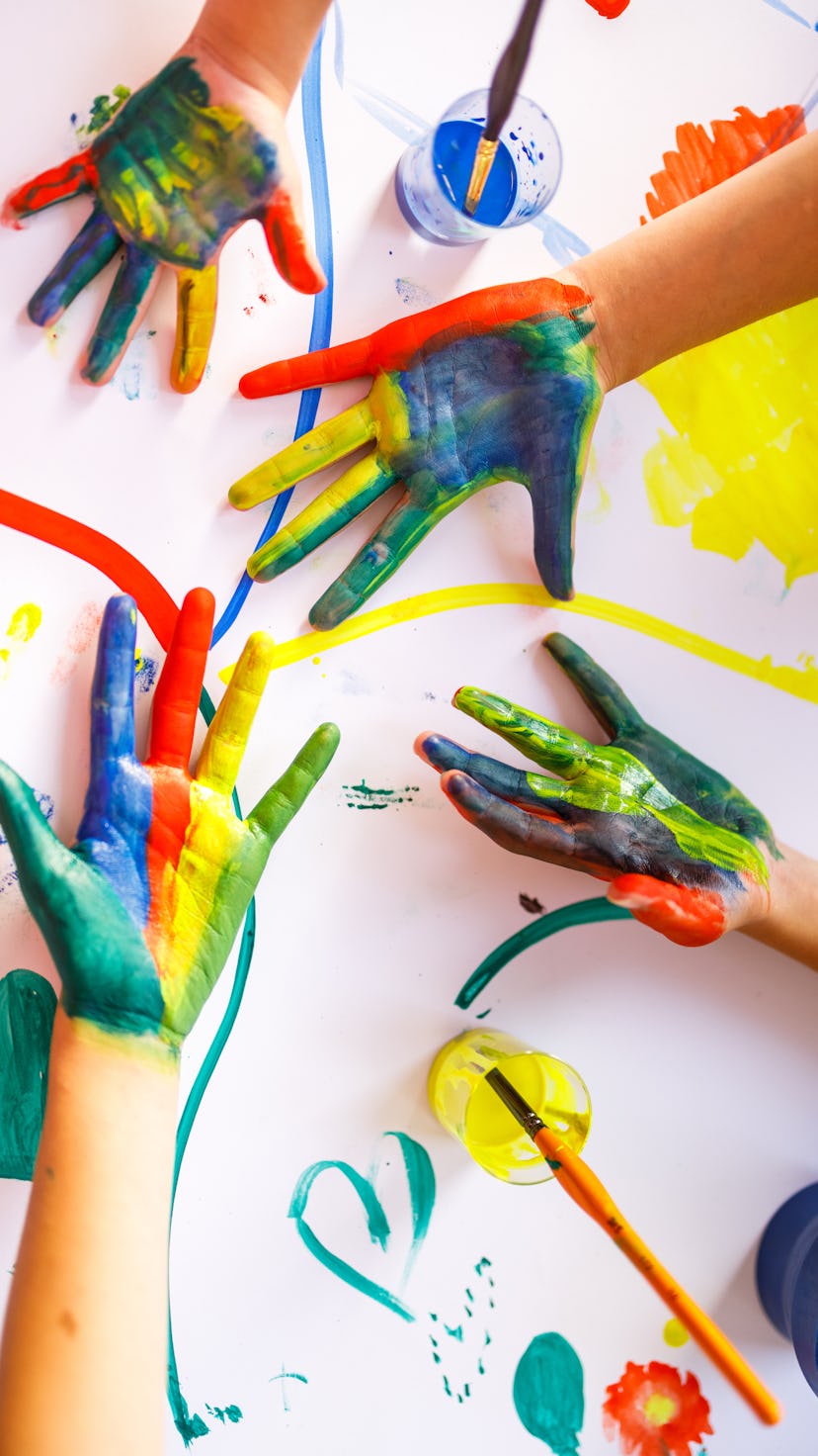 Children's hands with colorful paint on them, above a finger-painted background.