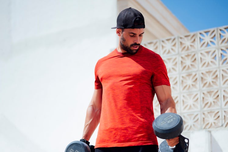 A man with big shoulders lifting weights outside.
