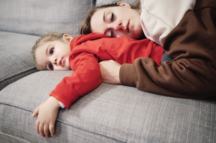 A mom sleeping on top of her daughter on a couch.
