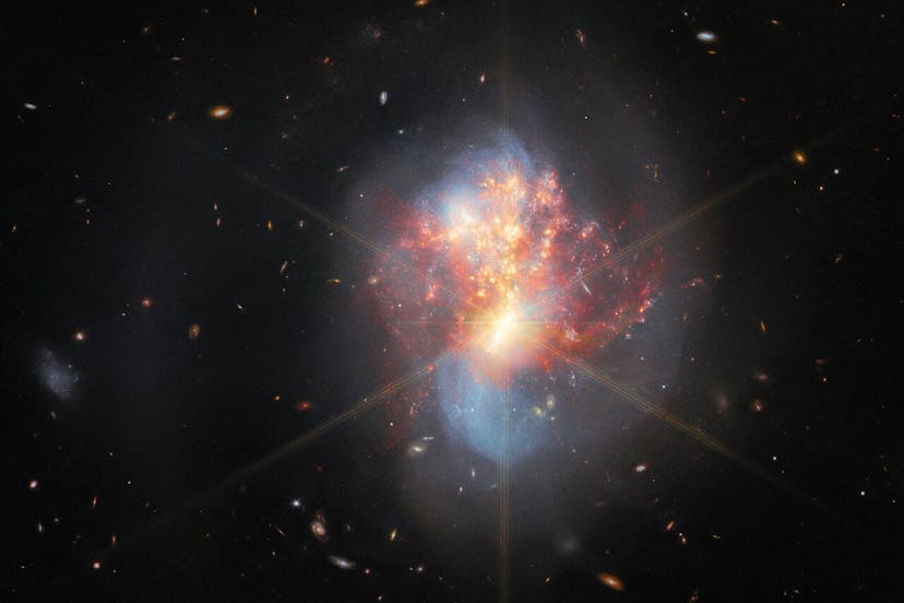 The two galaxies swirl into a single chaotic object in the centre. Long, blue spiral arms stretch ve...