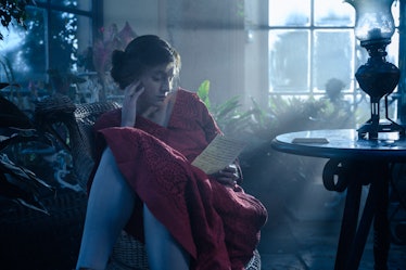 emma corrin in lady chatterly's lover wearing a red dress sitting in a chair reading