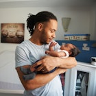 A father holding his baby in the child's bedroom, next to a crib.