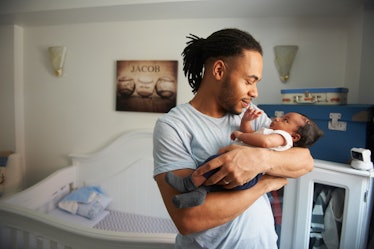 A father holding his baby in the child's bedroom, next to a crib.