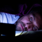 A man on his phone in bed in the dark.