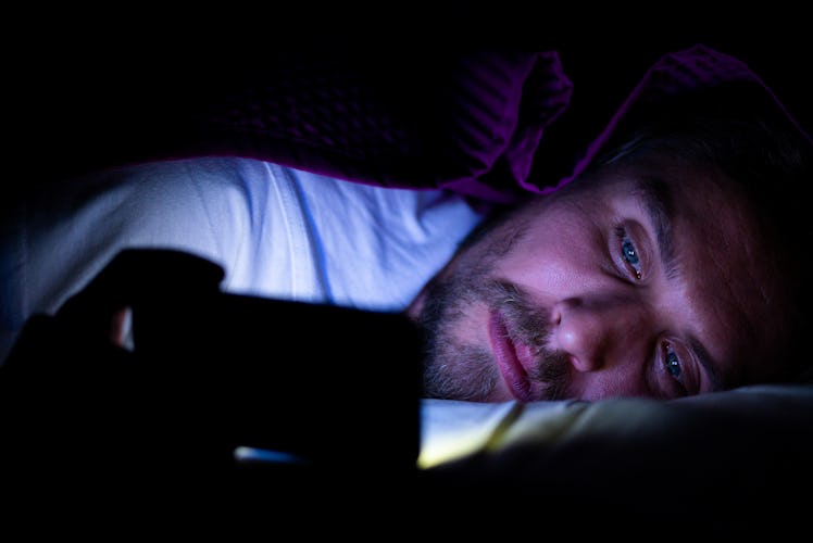 A man on his phone in bed in the dark.