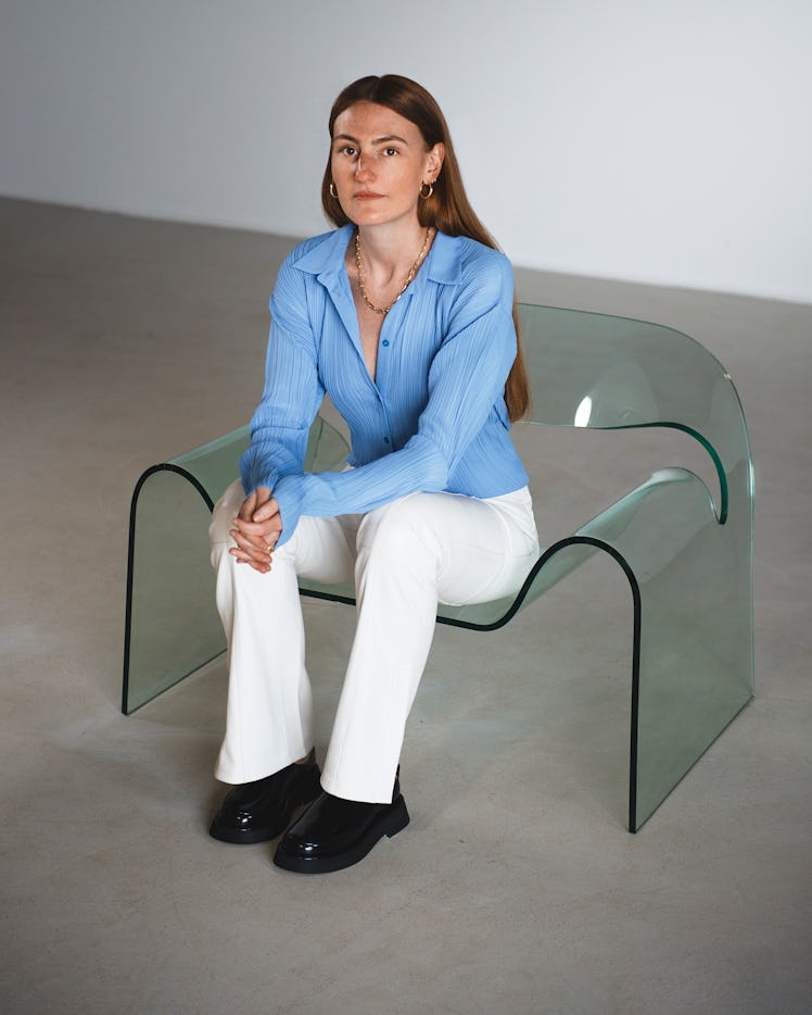 the designer Elza Wandler sitting on a clear acrylic chair with her hands clasped