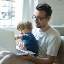 A man sits with his son and a laptop in his lap, his son pointing at the laptop screen.
