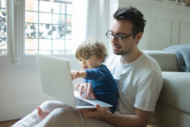 A man sits with his son and a laptop in his lap, his son pointing at the laptop screen.