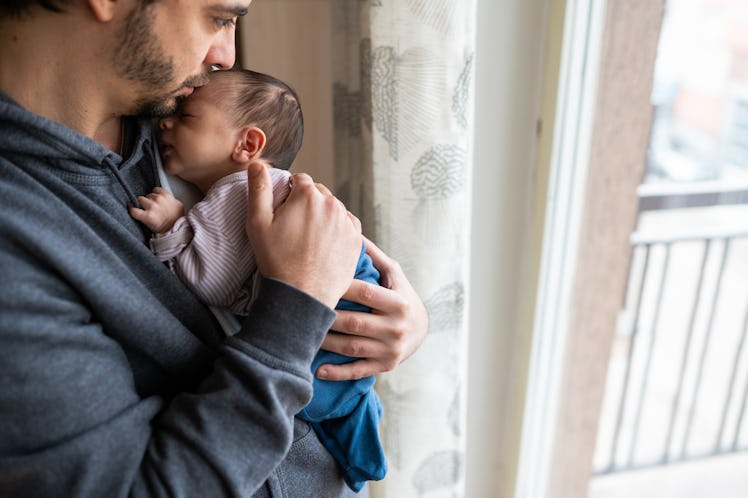A father holding his newborn at home and kissing their head.