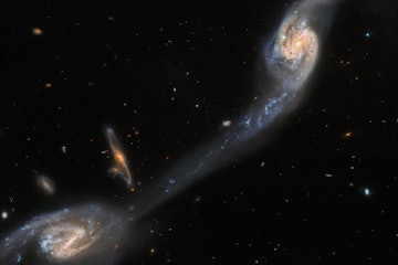 Two spiral galaxies are viewed almost face-on; they are a mix of pale blue and yellow in colour, cro...