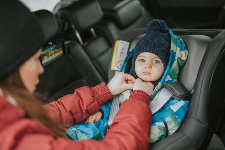 A mom putting a baby wearing a winter coat into a car seat.