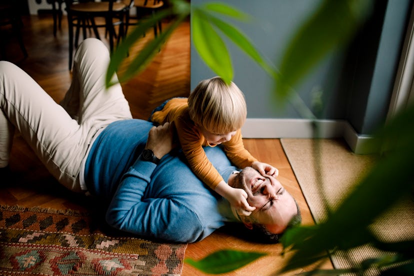 Father laying on ground and laughing while toddler pinches his cheeks