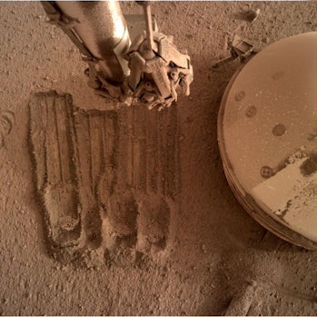 Trong một bức ảnh khác gần đây, InSight sử dụng cánh tay robot của mình để loại bỏ một số chu vi của regolith ...