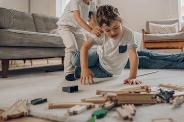 A child pushes their sibling at home while playing with toys.