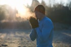 一个男人在寒冷的天气里，把看得见的呼吸吹到戴着连指手套的手上。