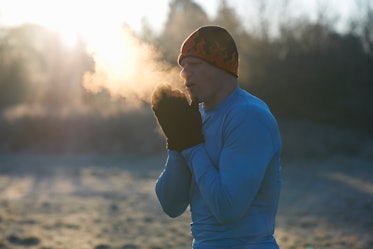 一个男人在寒冷的天气里，向他戴着连指手套的手上吹着明显的气息。