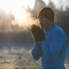 一个男人在寒冷的天气里，向他戴着连指手套的手上吹着明显的气息。