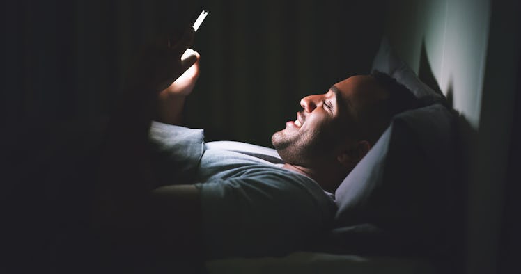 A man texting in the dark in bed.