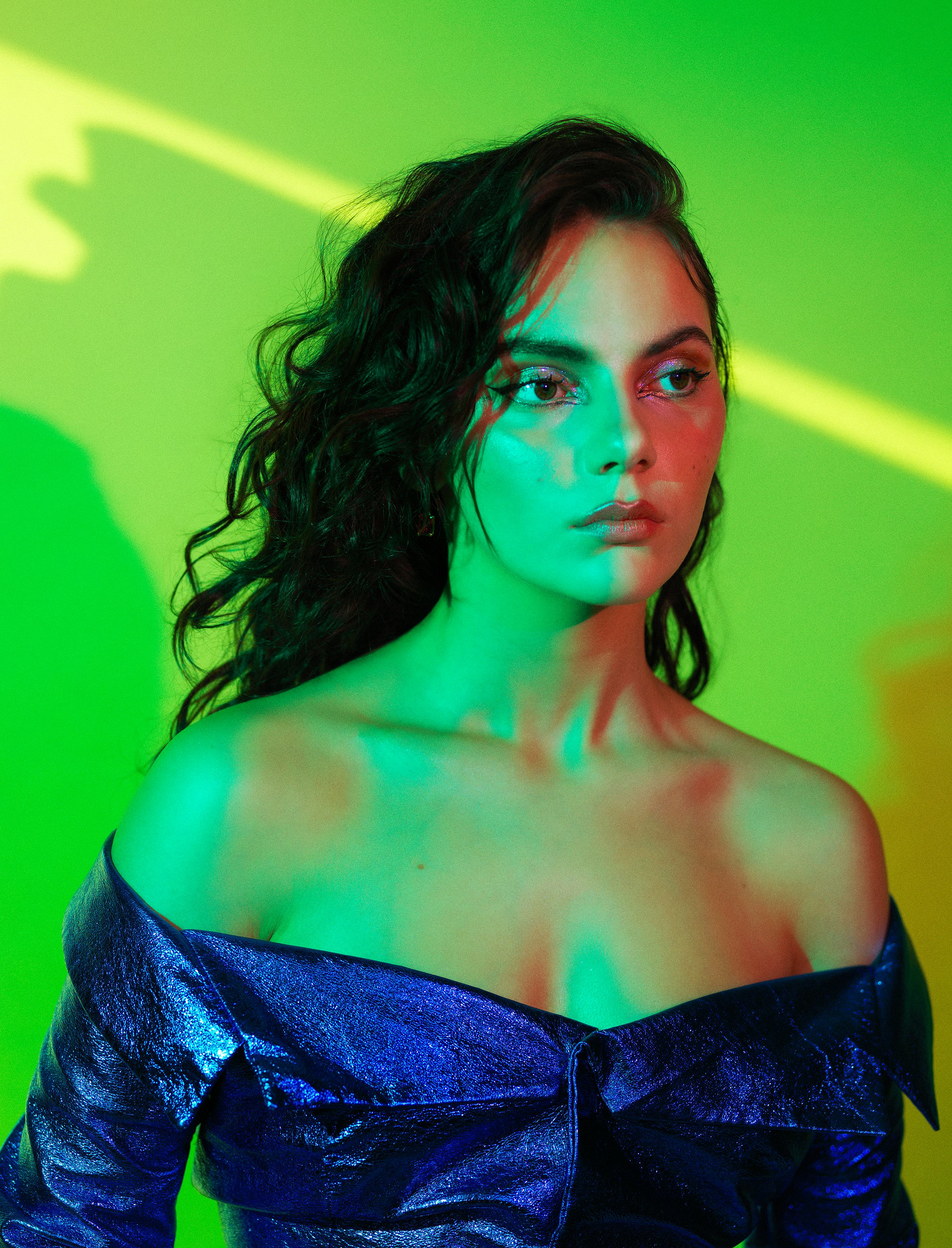 A portrait of Dafne Keen wearing a blue blouse, bathed in green light