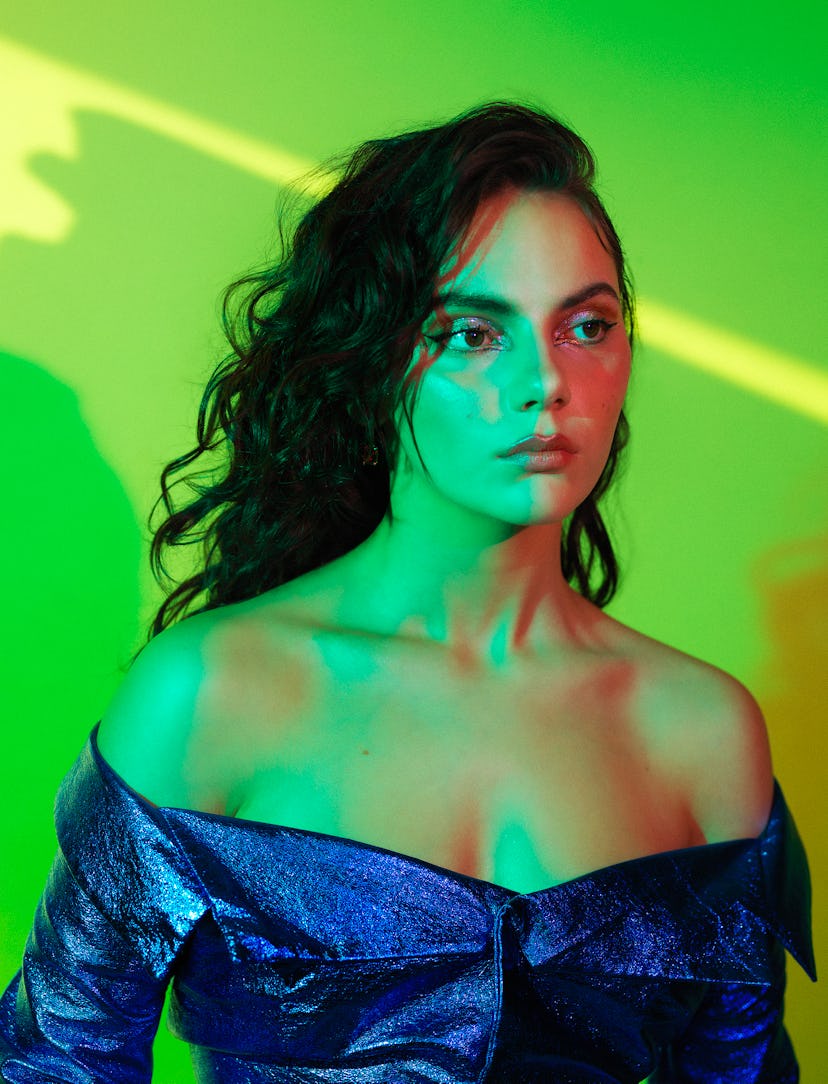 A portrait of Dafne Keen wearing a blue blouse, bathed in green light